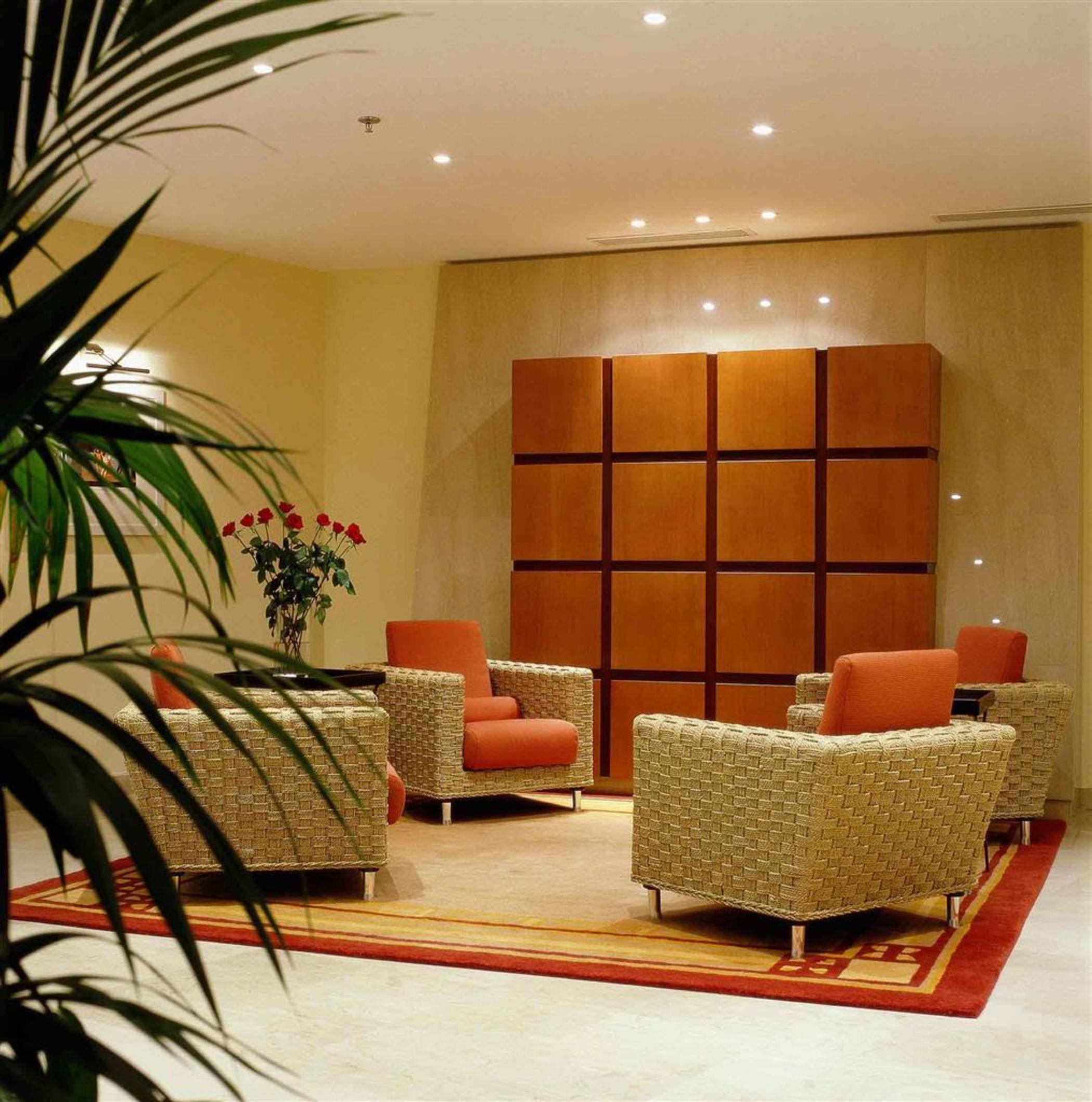 Sofitel Athens Airport Hotel Spata  Luaran gambar The photo shows a modern lounge area with a warm and inviting atmosphere. There are four chairs arranged around a central area, with two chairs upholstered in orange fabric and two in a woven material. A small decorative rug is placed under the seati