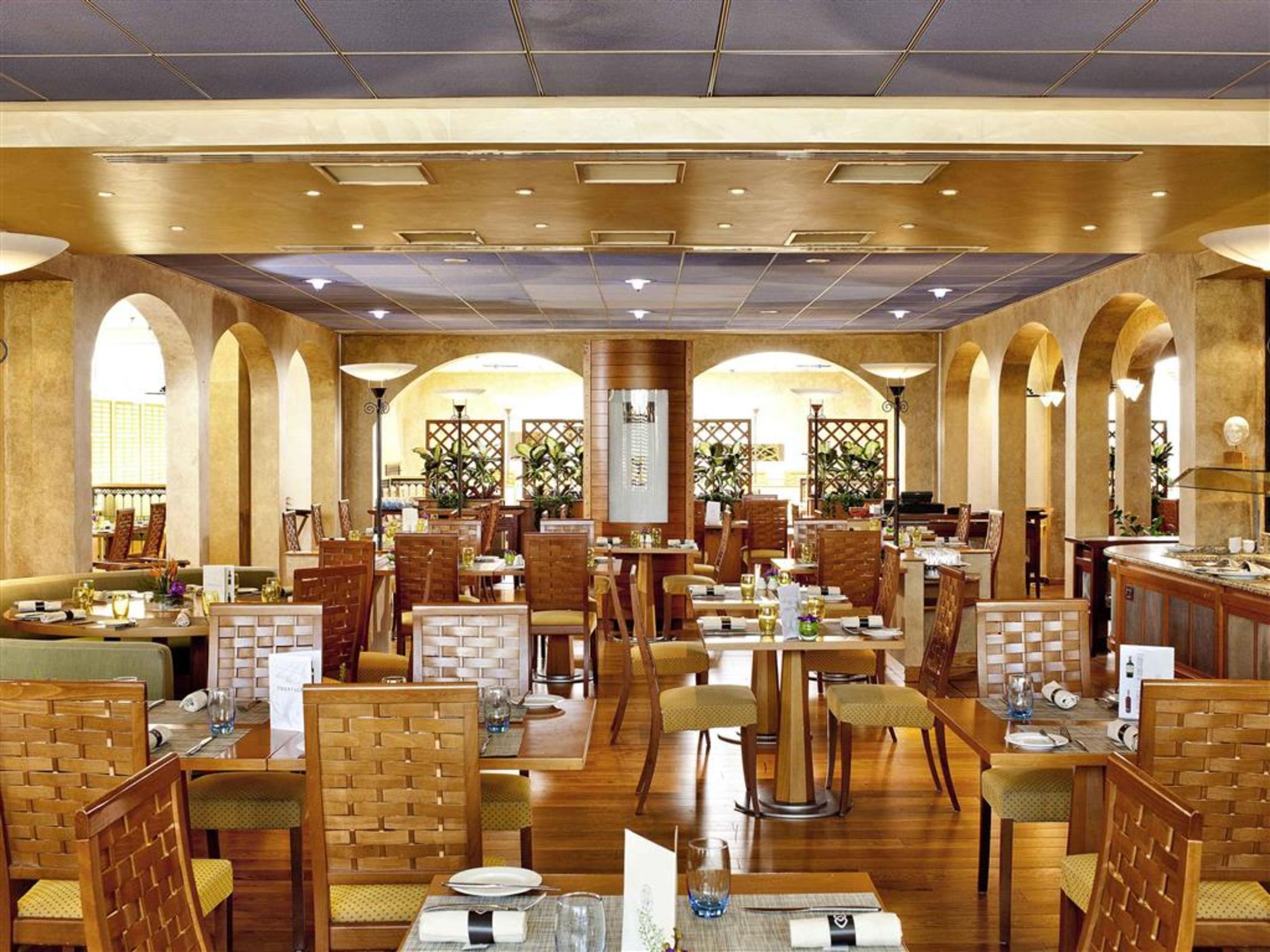 Sofitel Athens Airport Hotel Spata  Luaran gambar The photo shows the interior of a restaurant. The space features a warm and inviting design, with wooden flooring and elegantly arranged tables. Each table is set with tableware, and there are wooden chairs with a modern, simple design. The restauran