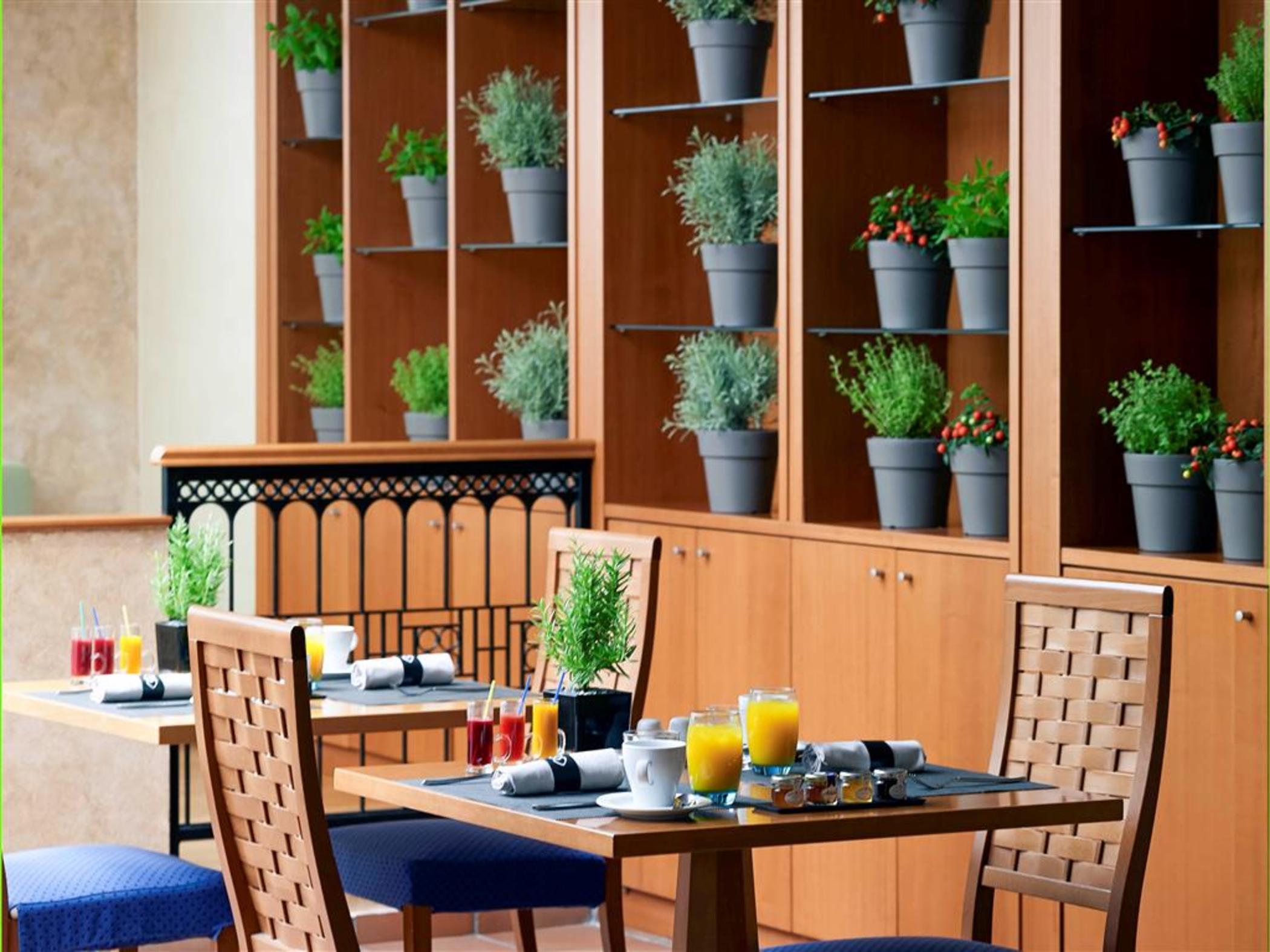 Sofitel Athens Airport Hotel Spata  Luaran gambar The photo depicts a cozy dining area, likely in a restaurant or hotel. There are wooden tables set with breakfast items, including glasses of fresh juice and other small dishes. The seating includes chairs with simple designs. Behind the tables, ther