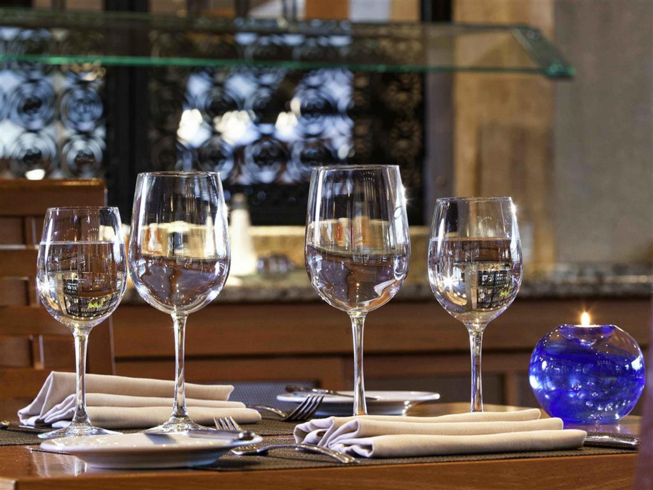 Sofitel Athens Airport Hotel Spata  Luaran gambar The photo shows a dining table set with four elegant wine glasses filled with water. The glasses are positioned in a row on the table. Next to each glass, there are neatly folded napkins and forks. There is also a small blue decorative candle holder 