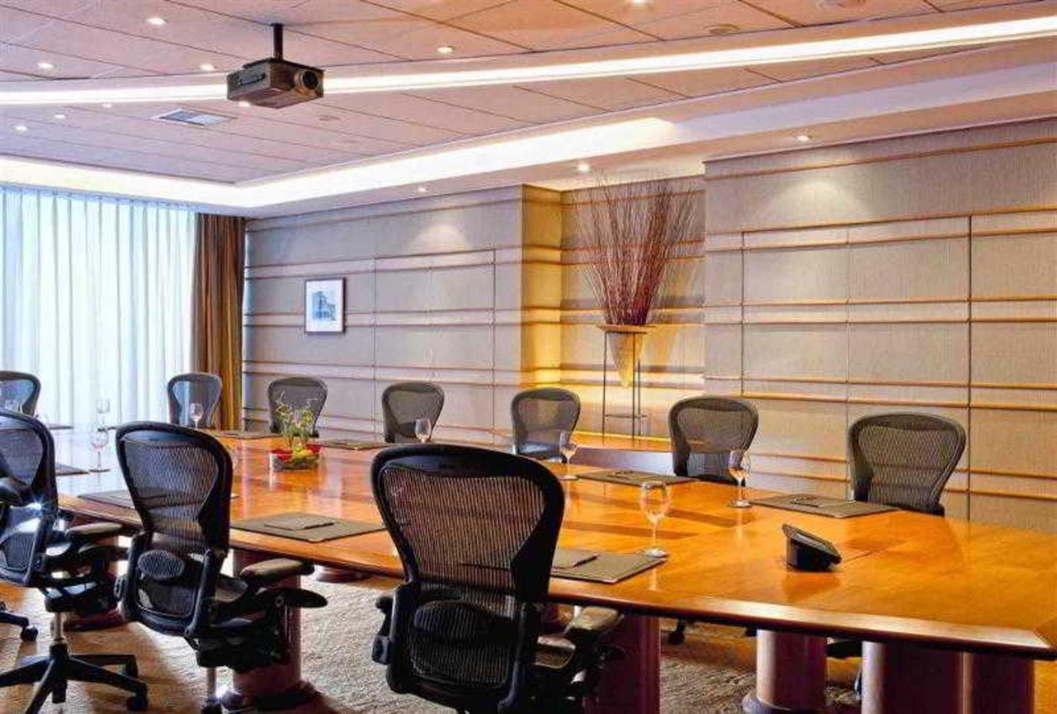 Sofitel Athens Airport Hotel Spata  Luaran gambar The photo shows a modern conference room. It features a long wooden table surrounded by ergonomic office chairs. The room is well-lit with recessed lighting and has a projector hanging from the ceiling. Large windows allow natural light to enter, wit