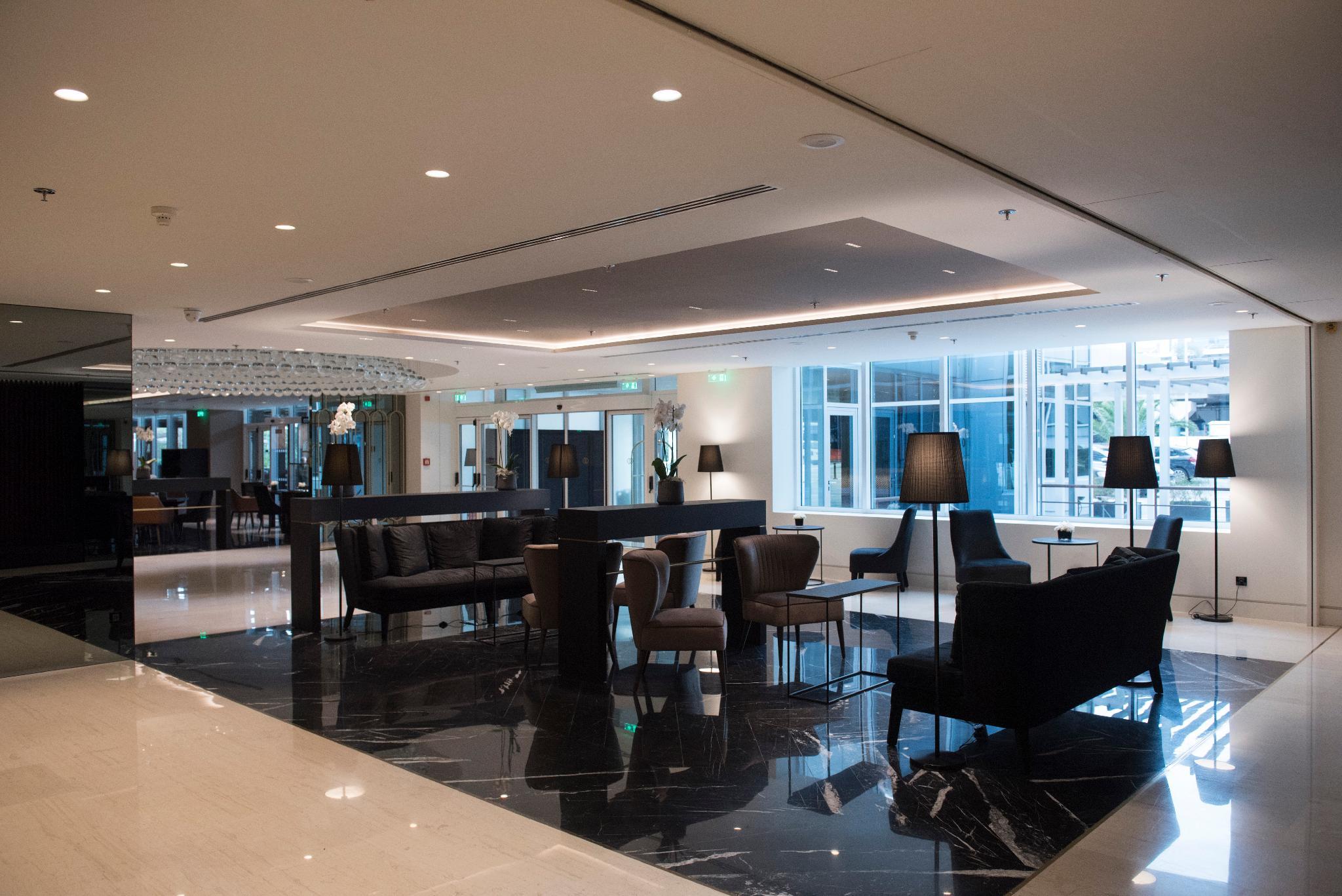 Sofitel Athens Airport Hotel Spata  Luaran gambar The photo shows a modern lobby or lounge area. It features sleek, contemporary furniture including black leather sofas and chairs, paired with elegant tables. The flooring appears to be dark marble, adding a touch of luxury. The space is well-lit wit