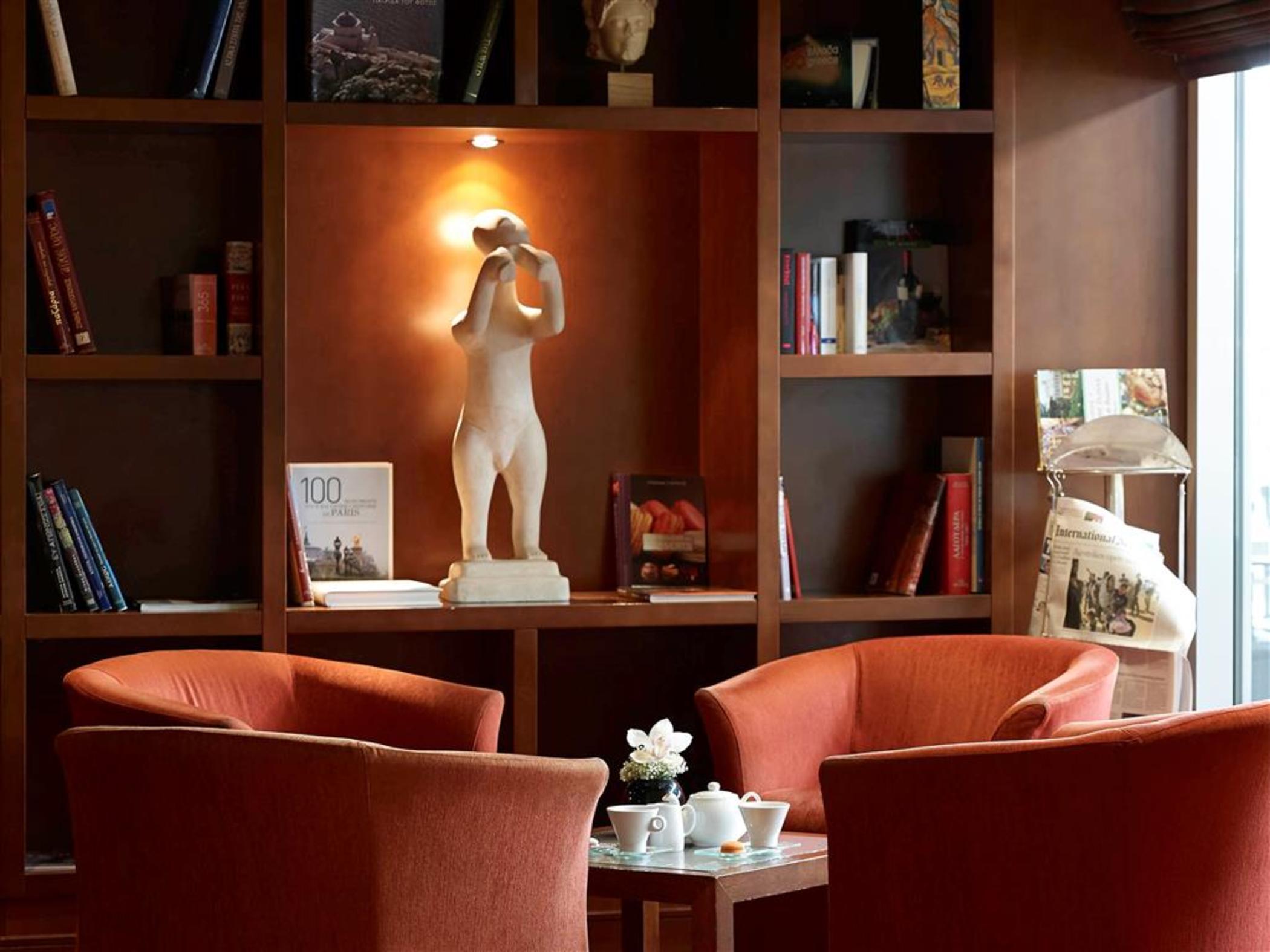 Sofitel Athens Airport Hotel Spata  Luaran gambar The photo shows a cozy interior space, likely a lounge or reading area. In the center, there are two orange chairs facing each other, around a small table. On the table, there appears to be a teapot and teacups, along with a small flower arrangement.