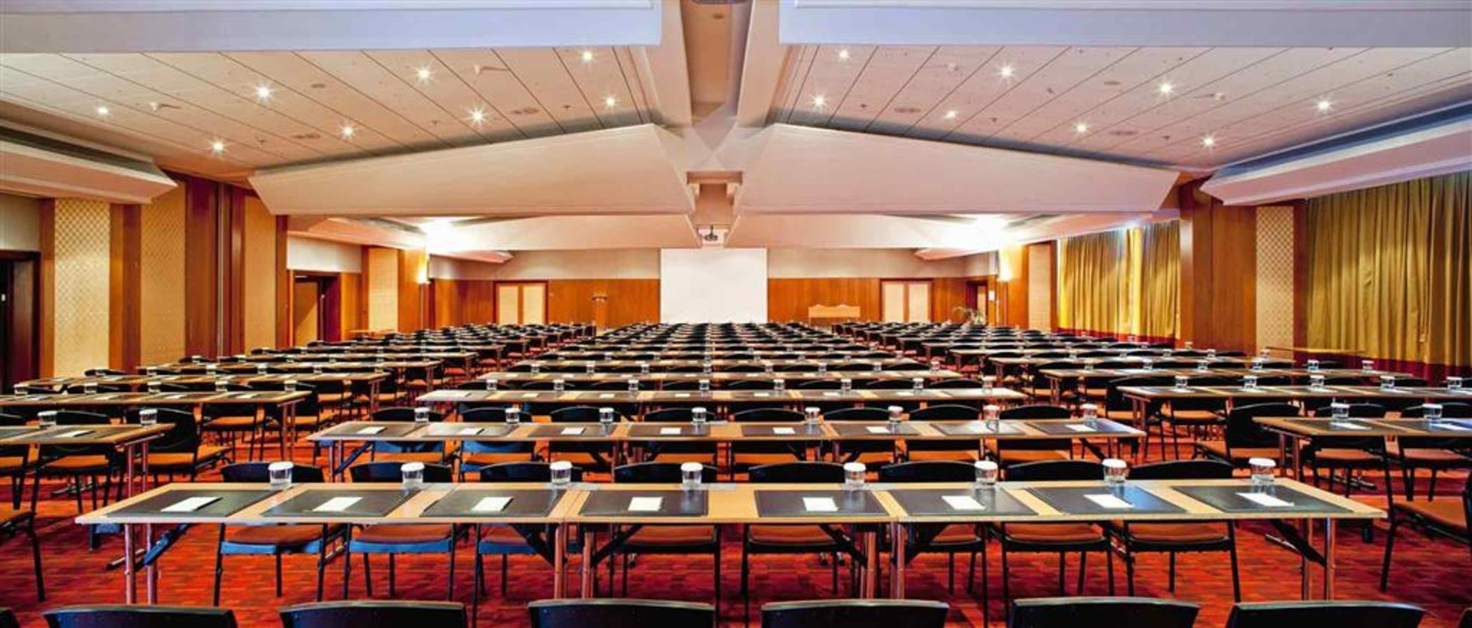 Sofitel Athens Airport Hotel Spata  Luaran gambar The photo shows a large conference room setup. The room is arranged with numerous tables organized in rows, facing a central presentation area. Each table has a notepad and a glass of water. There is a large blank white screen positioned at the front