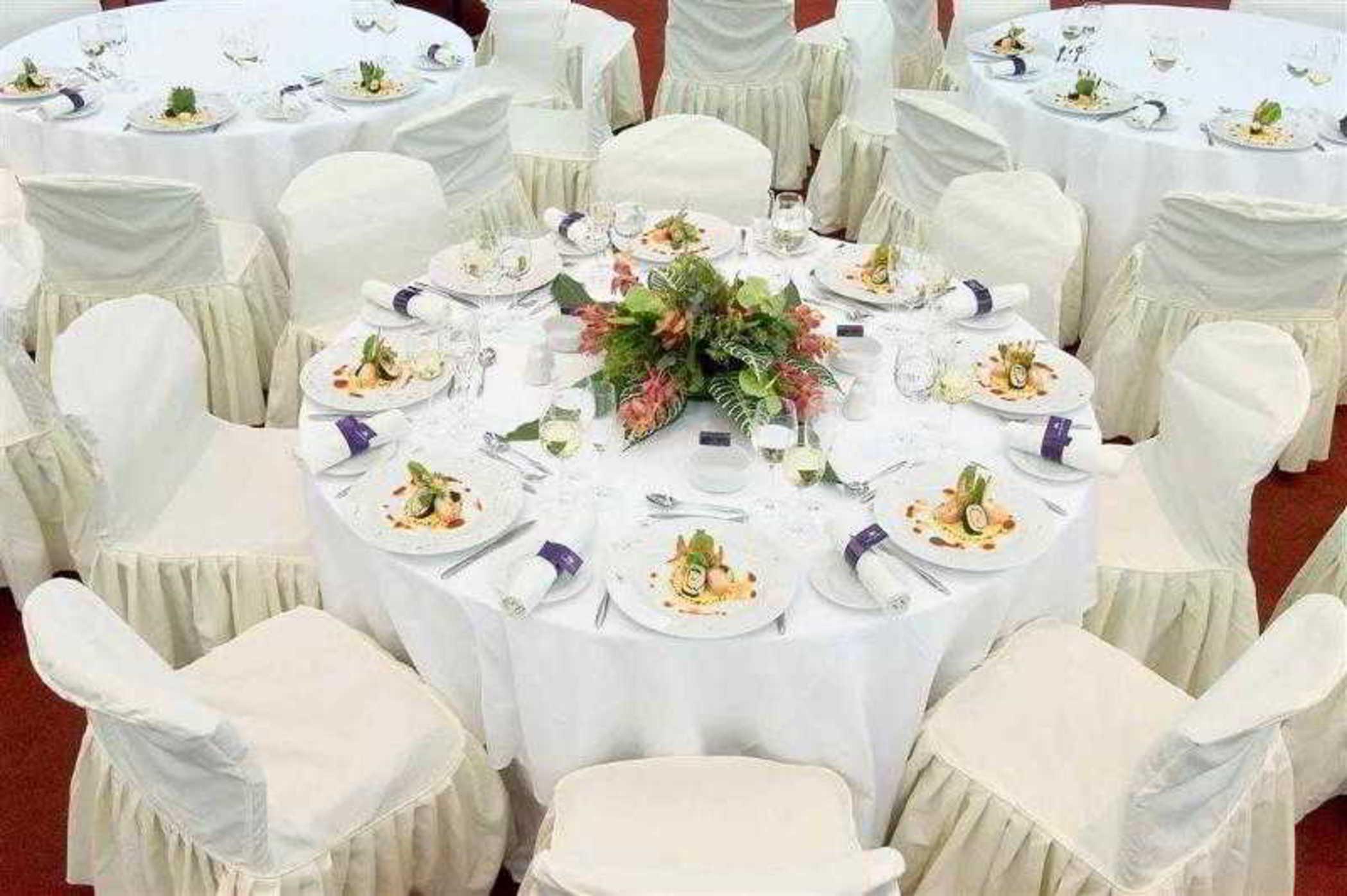 Sofitel Athens Airport Hotel Spata  Luaran gambar The image shows a beautifully arranged dining setup. There are several round tables covered with white tablecloths, and each table is surrounded by white chairs, likely dressed in covers that drape to the ground. 

On each table, there are elegant pl