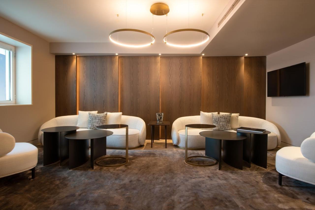 Sofitel Athens Airport Hotel Spata  Luaran gambar The photo shows a modern and stylish interior space designed for relaxation or social gatherings. It features two curved white sofas positioned around small, round black tables. The walls are adorned with dark wooden panels, providing a warm contrast