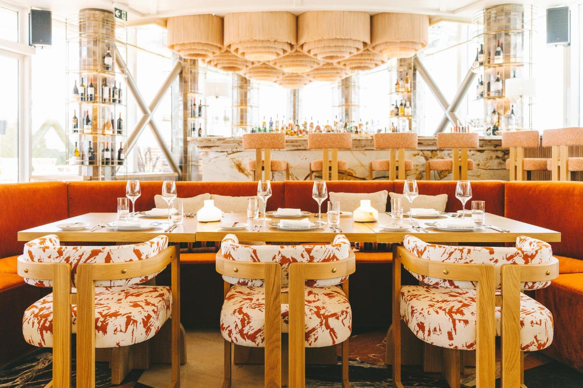 Sofitel Athens Airport Hotel Spata  Luaran gambar The photo depicts a stylish restaurant interior. It features a modern design with a warm color palette. In the foreground, there are several dining tables surrounded by unique chairs that have a vibrant floral pattern. The chairs are made of wood wit