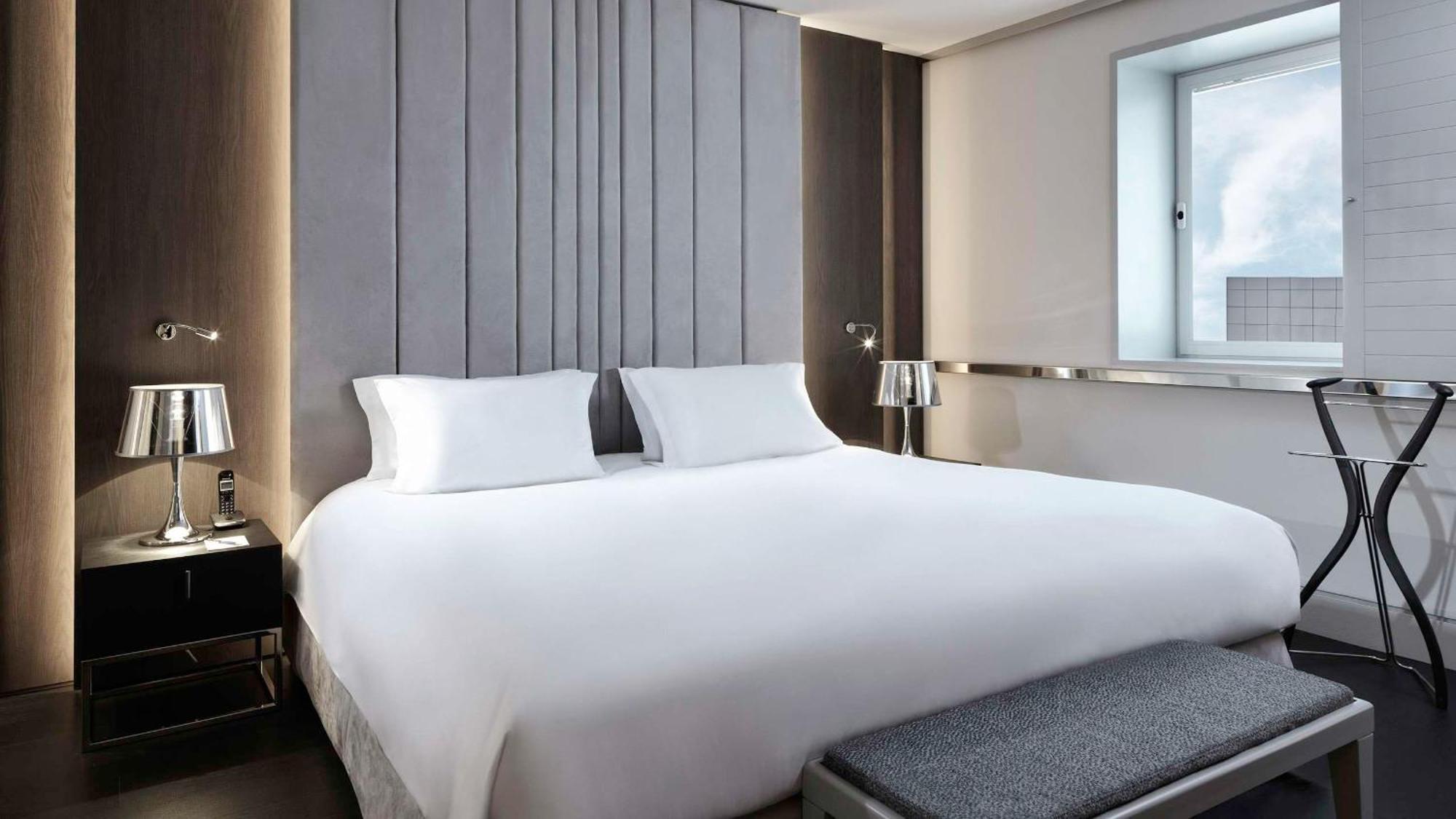 Sofitel Athens Airport Hotel Spata  Luaran gambar The photo shows a modern hotel room featuring a large bed with white linens and two white pillows. The headboard has a sleek, vertical design, adding a contemporary touch to the room. On either side of the bed, there are stylish bedside tables with t