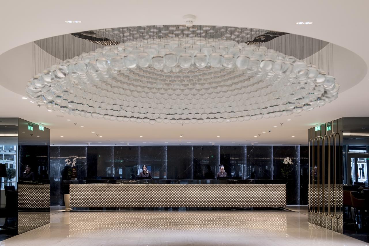 Sofitel Athens Airport Hotel Spata  Luaran gambar The photo shows a modern hotel lobby. The centerpiece is an impressive, artistic chandelier made of glass, which hangs from the ceiling and features a circular design. Below the chandelier, there is a reception desk, which is sleek and stylish, likel