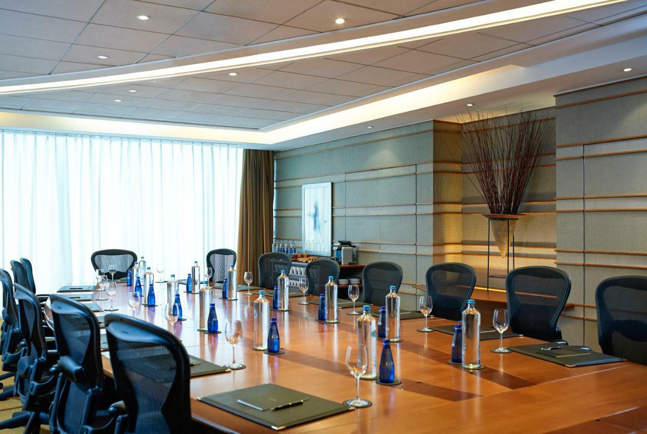 Sofitel Athens Airport Hotel Spata  Luaran gambar The photo shows a conference room featuring a long wooden table surrounded by black ergonomic chairs. Each place at the table is set with a notepad and a pen. There are several blue glass water bottles positioned at intervals along the table, alongsi